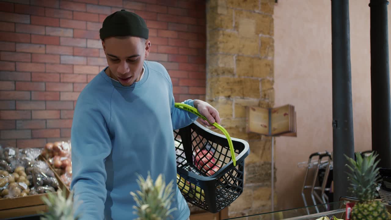 Mladý atraktivní muž smíšené rasy si vybírá produkty v supermarketu a vkládá je do košíku.