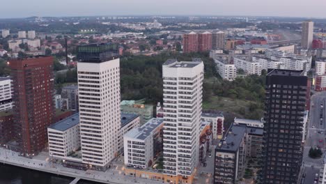 drone footage of four high-rise residential buildings with modern design and architecture in årstadal, stockholm during sunset with apartment buildings in background