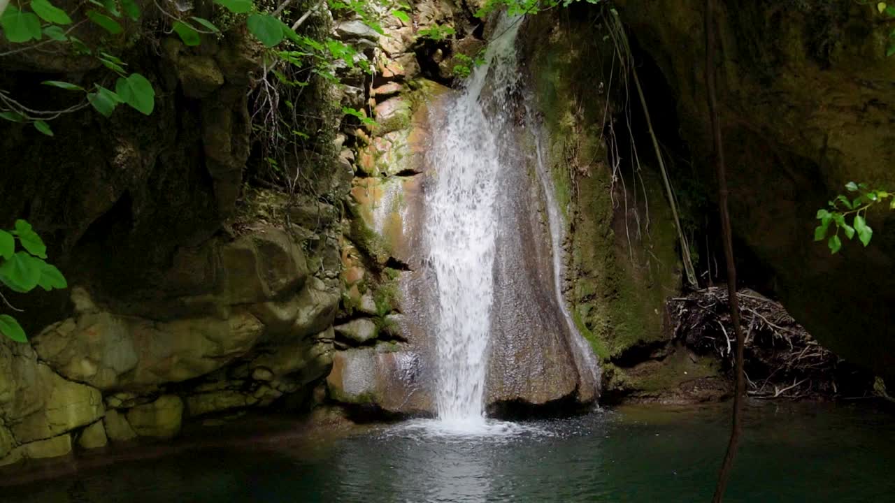 cámara lenta de la cascada de kefalogourna, rodeada de vegetación verde y rocas musgosas, la luz del sol brillando, isla de thassos, grecia