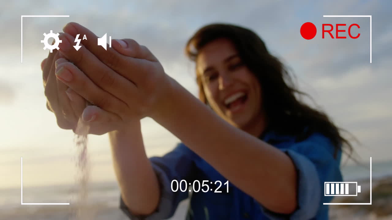 sosteniendo arena y sonriendo, mujer en la playa con animación de grabación de cámara