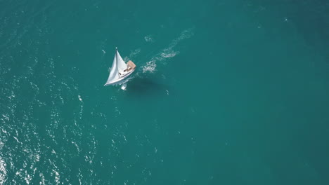 sailboat sailing underway, filmed from a drone above looking almost straight down onto the beautiful blue water.