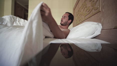 waking up angrily to morning alarm naked in luxurious hotel bed