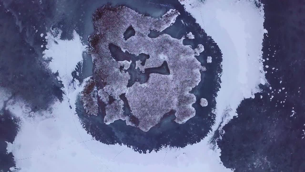 Aerial birdseye view of frozen lake Liepaja during the winter, blue ice with cracks, dry yellowed reed islands, overcast winter day, wide orbiting drone shot