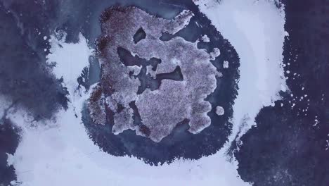 aerial birdseye view of frozen lake liepaja during the winter, blue ice with cracks, dry yellowed reed islands, overcast winter day, wide orbiting drone shot