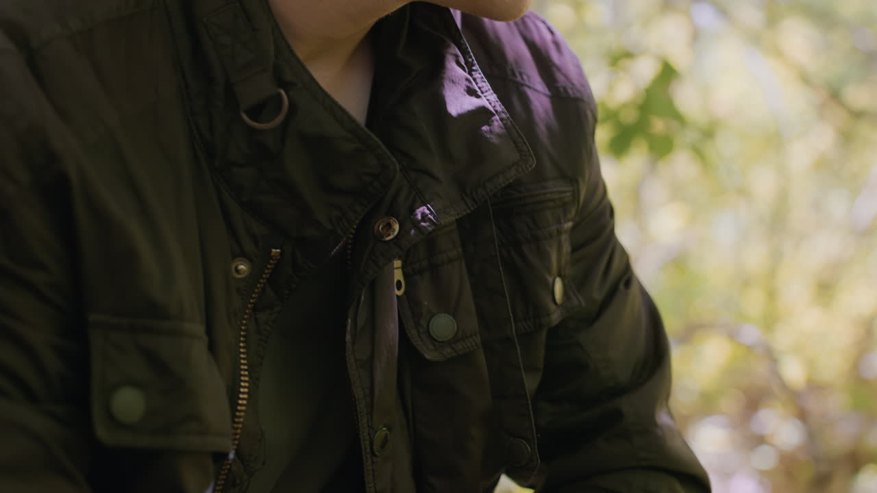 Close-view of young tourist adjusting belt and putting on jacket, rolling sleeves up in readiness to face any danger while in the middle of the forest for an outdoor adventure in nature