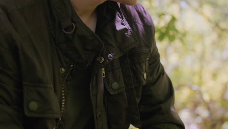 close-view of young tourist adjusting belt and putting on jacket, rolling sleeves up in readiness to face any danger while in the middle of the forest for an outdoor adventure in nature