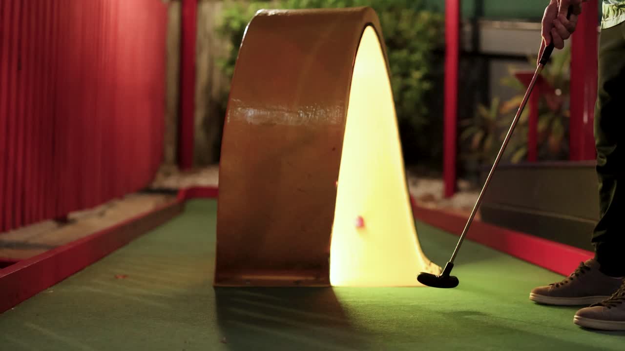 un jugador intenta un putt de mini golf en una rampa brillante bajo una iluminación cálida, capturando la esencia de la diversión y el desafío