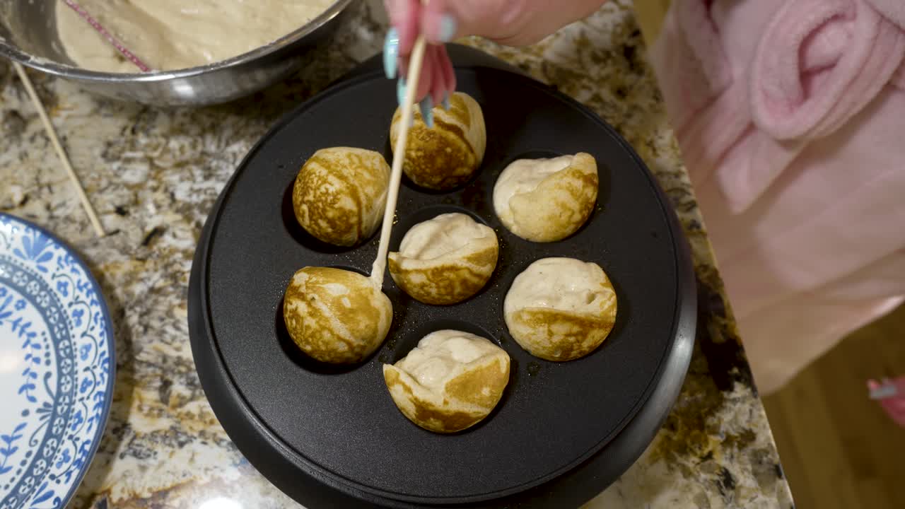 volteando los aebleskivers en una sartén caliente para que se cocinen uniformemente - vista superior de la serie aebleskiver