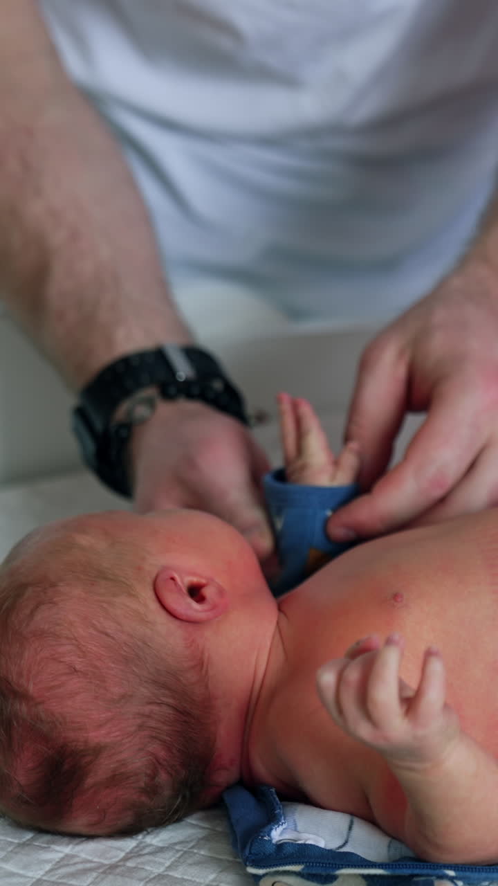 Healthy Caucasian newborn lies on the table. Child is dressed by his parents. Top view. Vertical video