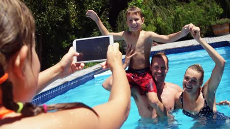 girl taking photo of family on mobile phone near poolside