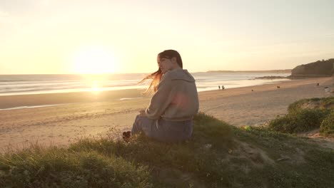 Mujer-Viajera-Sentada-En-Una-Colina-Contra-El-Cielo-Del-Atardecer-Cerca-Del-Mar