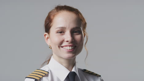 studio portrait of smiling female airline pilot or ship captain against plain background