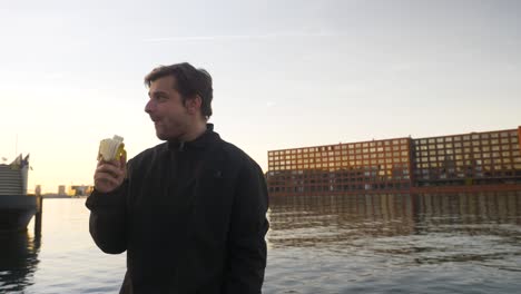 wide shot of a young man eating a banana and rejoicing on a pier during sunset