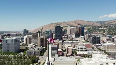 Bandera-Americana-Ondeando-Con-El-Horizonte-Del-Centro-De-Salt-Lake-City,-órbita-Aérea