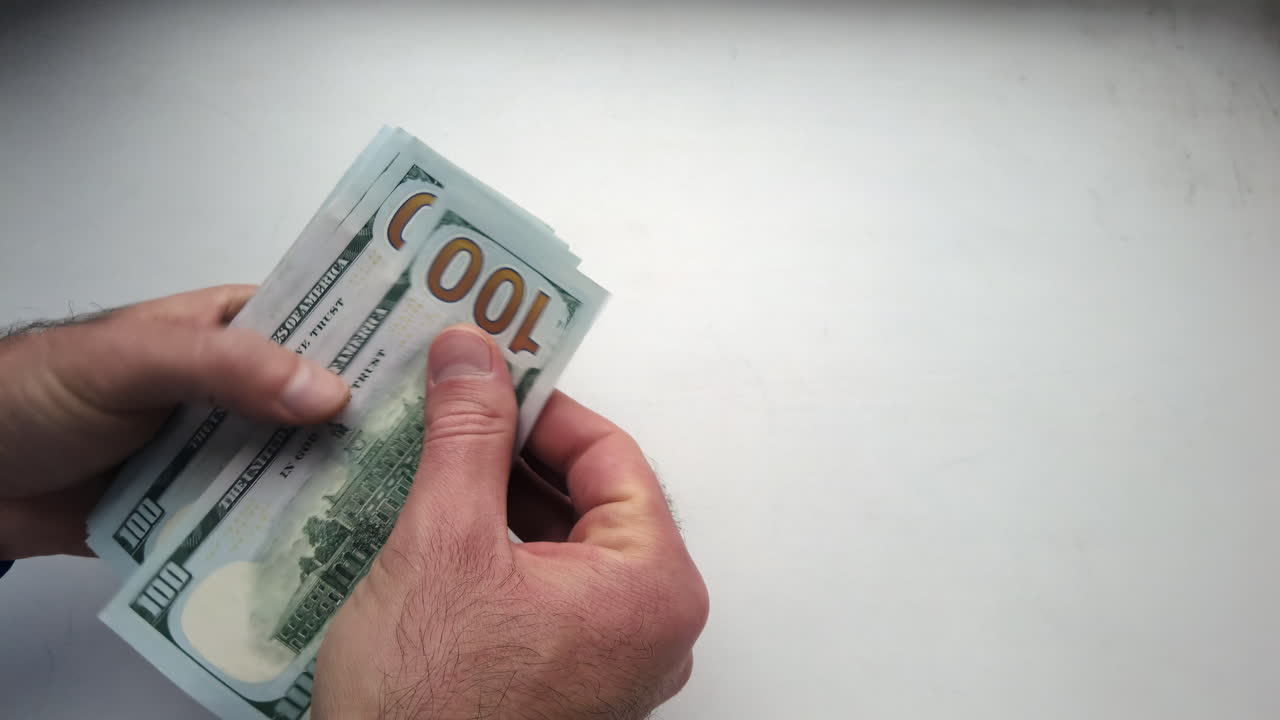 Hands are seen counting several hundred dollar bills on a simple white background, showcasing careful handling of cash in a calm setting