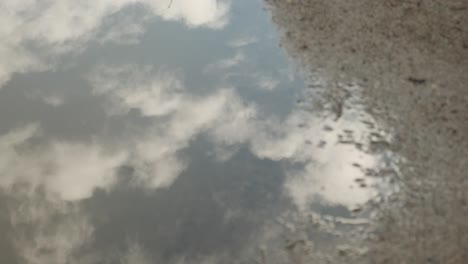 reflections of sky and moving clouds in puddle