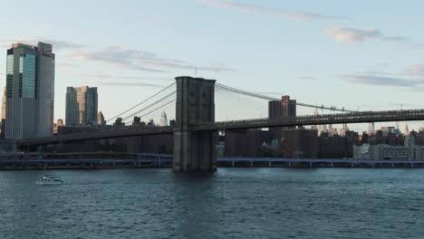 wide angle aerial tracking shot of the brooklyn bridge with downtown lower manhattan, new york city in the background at dusk on a clear summer evening