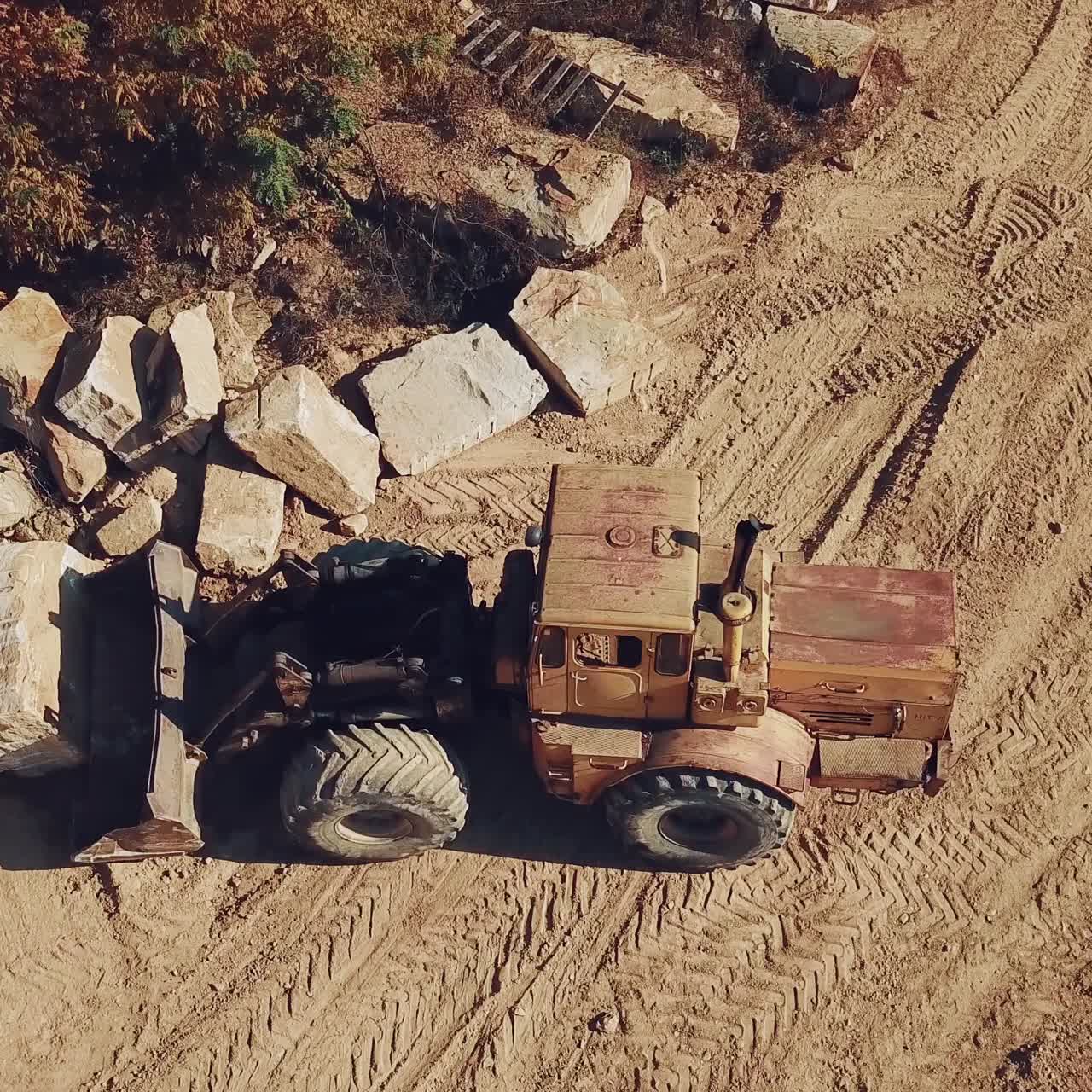 yellow bulldozer with a bucket is carrying a large stone near a sand quarry. Camera motion down. Close-up