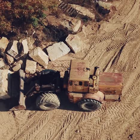 yellow bulldozer with a bucket is carrying a large stone near a sand quarry. camera motion down. close-up