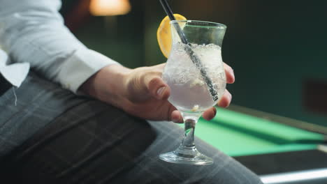 close-up of person, face not visible, wearing white shirt and grey trousers, holding glass of lemon drink with black straw. ice cubes and lemon slice add refreshing detail in elegant setting