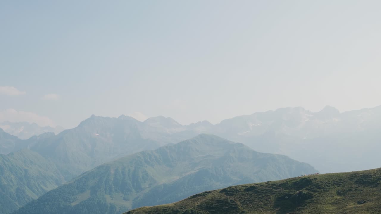 澄み切った空の下、なだらかな緑の丘と遠くの峰々が広がる山脈の眺め