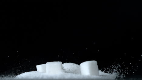 cubos de azúcar cayendo en una pila de azúcar sobre un fondo negro