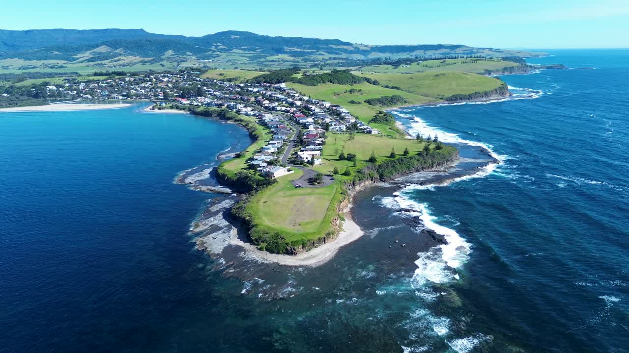 Drone aerial landscape of Gerroa headland and rugged rocky coastline with ocean reef waves and residential rural town homes along main road street on the South Coast Australia travel vacation tourism