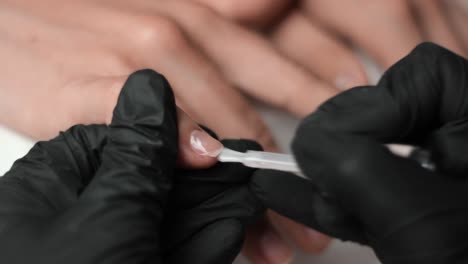 Beautician-wearing-gloves-painting-a-base-coat-onto-a-clients-hands-for-a-manicure