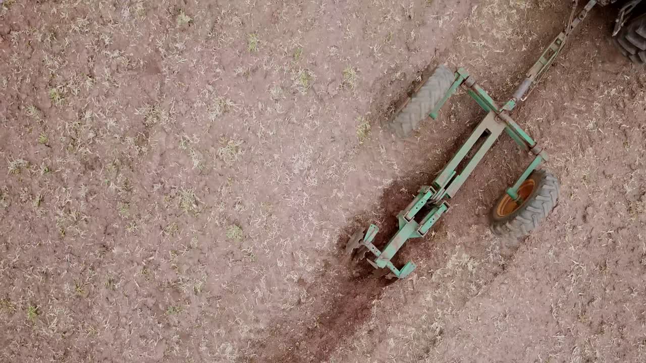 Veduta aerea dall'alto di un agricoltore su un trattore che coltiva il terreno. L'aratro lavora la terra, preparando il terreno fertile per la semina primaverile.