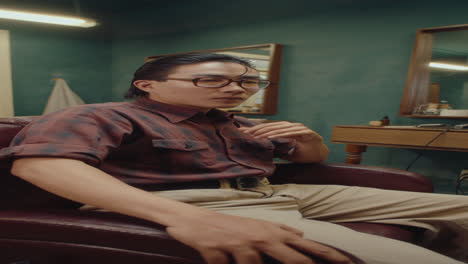 Well-Groomed Asian Man Sitting in Barbershop Chair Posing on Camera