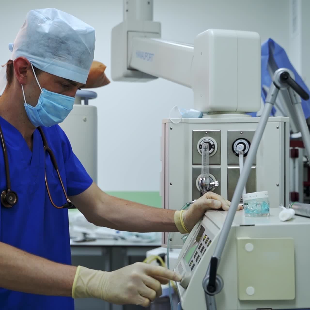 Medic in blue uniform with stethoscope on his shoulders switching on the equipment. Doctor pressing keys on the apparatus