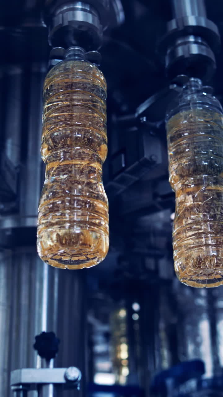 Cooking oil production. Plastic bottles filling with olive oil inside the modern factory. Automated machine moving on a circle way with refined oil. View from below. Vertical video