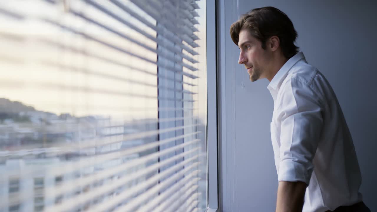 Side view of thoughtful young Caucasian male executive standing near window in modern office 4k