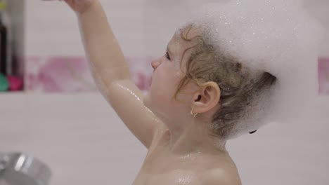 attractive three years old girl takes a bath. cute blonde child