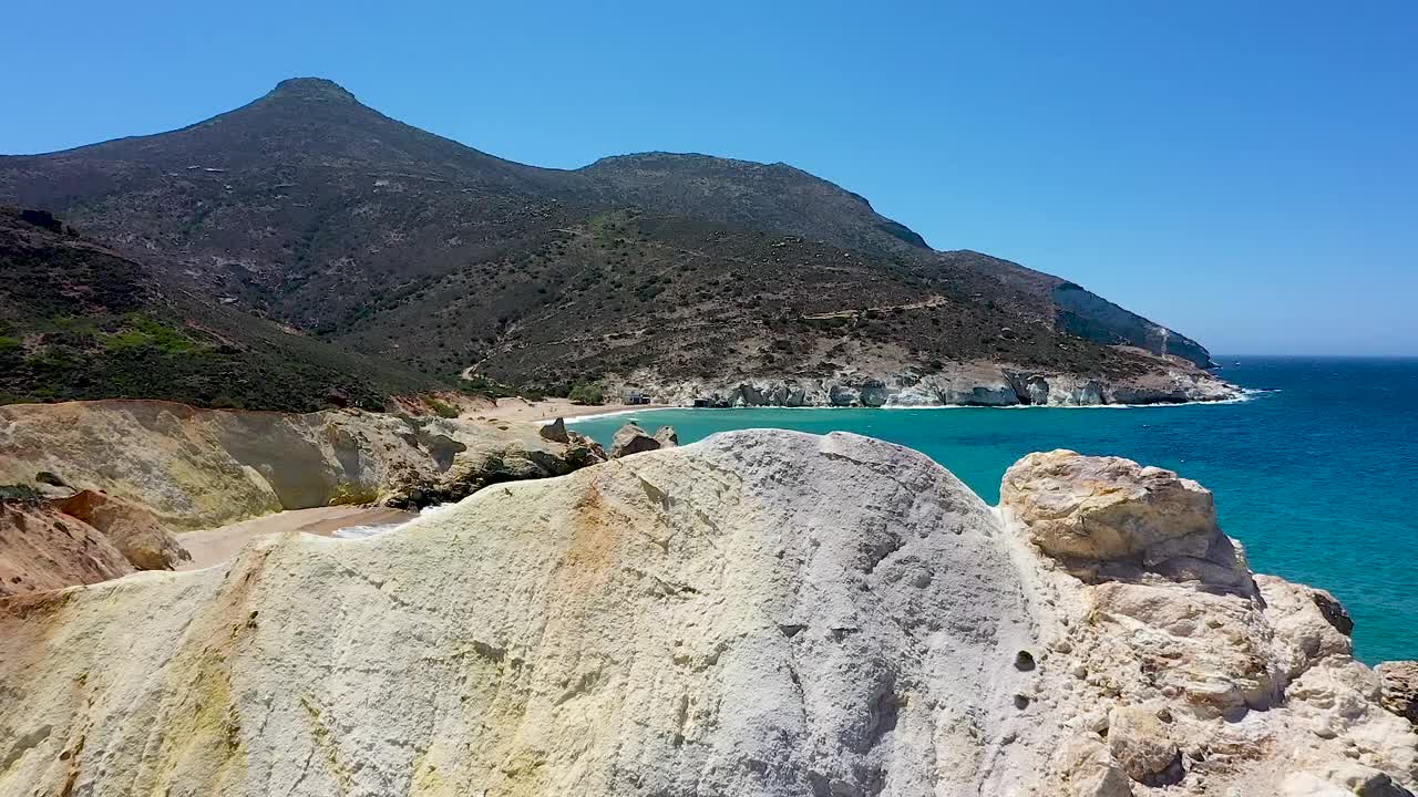 toma aérea de drones volando sobre piedras sulfúricas blancas y amarillas que revelan una playa de arena blanca con aguas turquesas exóticas y montañas detrás