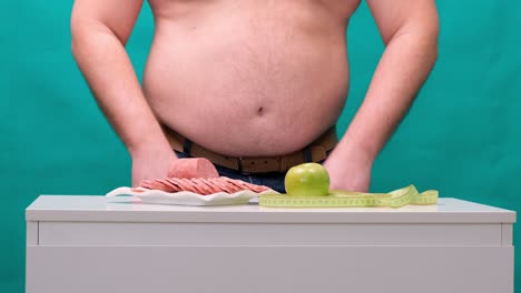 man with a fat belly chooses between sausage and a green apple. the concept of diet and willpower