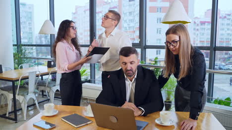 active and busy working day in office. boss in front of laptop and female standing next to him discussing issues in computer. man and woman having discussion at the background.