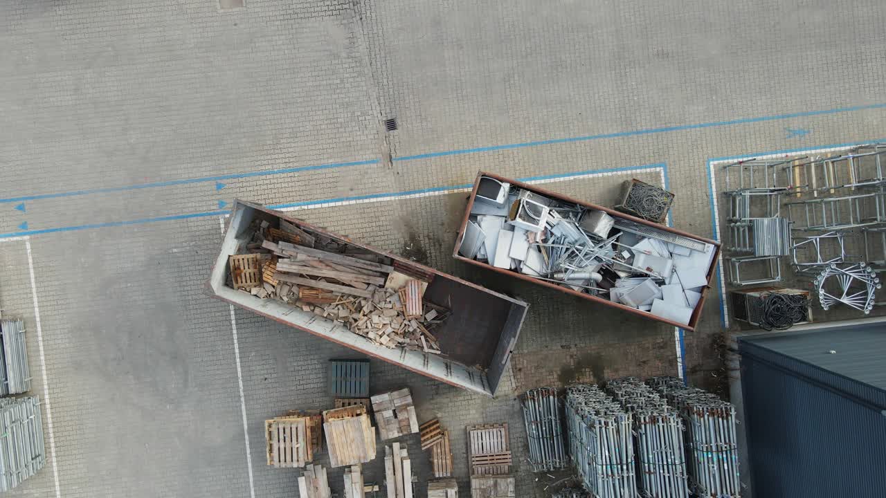Top down aerial of sorted materials placed in containers for recycling. The drone slow ascends to the wood and metal trash containers