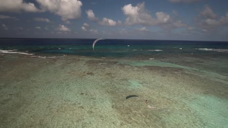 un kitesurfista se desliza a través de las aguas azules cristalinas de los rocas bajo un cielo brillante