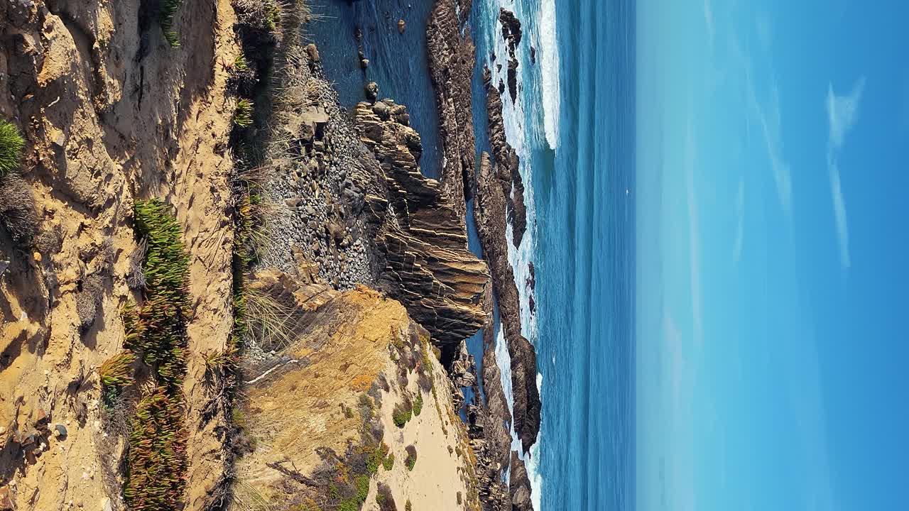 playa de praia de almograve con olas del océano, acantilados y piedras, arena dorada húmeda y vegetación verde en la costa salvaje de rotha vicentina, odemira, portugal