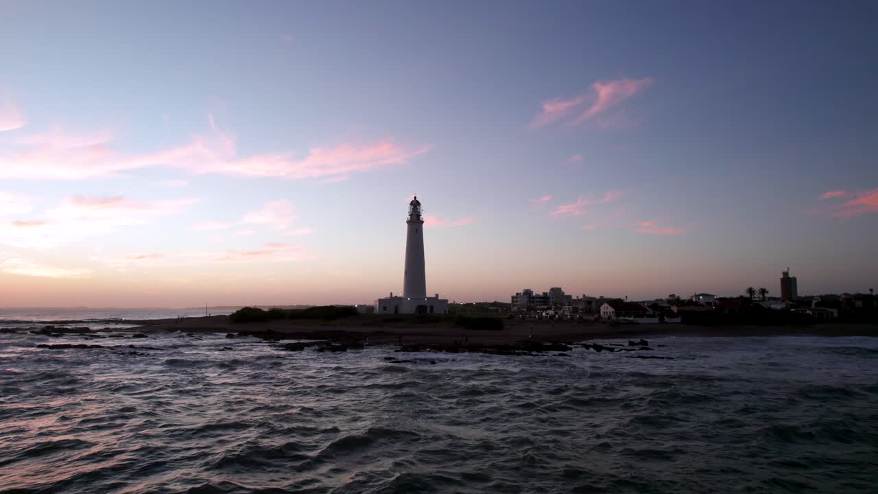 포르투갈의 파롤 섬에 있는 등대, 해가 지는 하늘을 배경으로 해변에 파도가 부히고 있다.