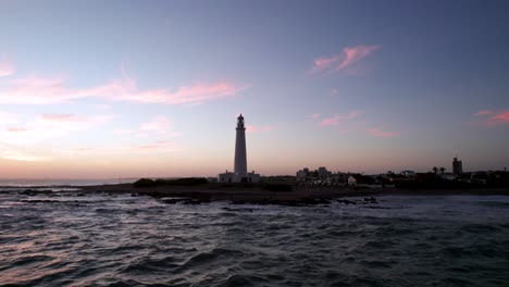 Faro-En-La-Isla-Farol,-Portugal-Contra-El-Cielo-Del-Atardecer,-Olas-Rompiendo-En-La-Costa