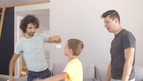 padres gay alegres enseñando a su hijo a bailar en casa
