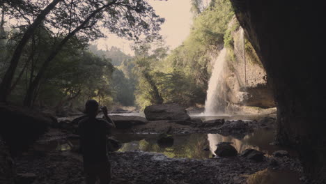 un joven fotógrafo de aventuras y naturaleza tomando fotos de una cascada desde una cueva en medio de la selva