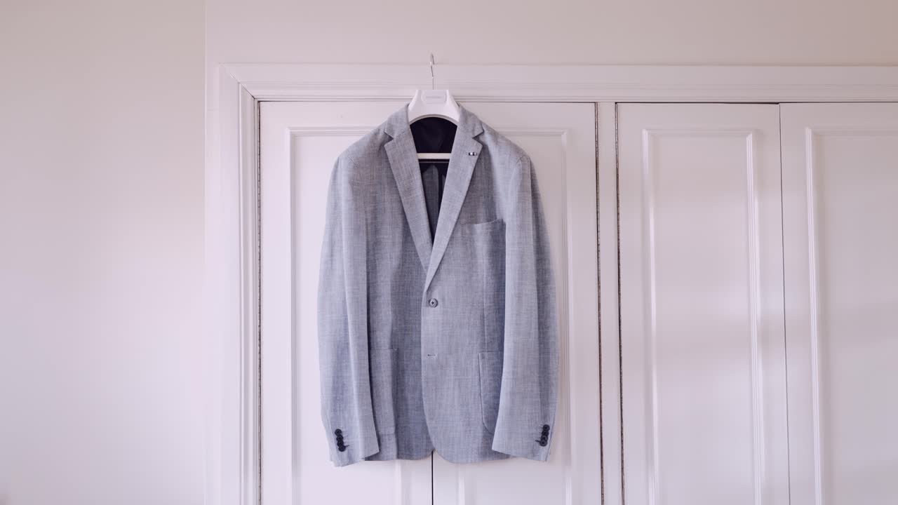 Elegant light gray suit jacket neatly hung on a white door in a minimalist setting