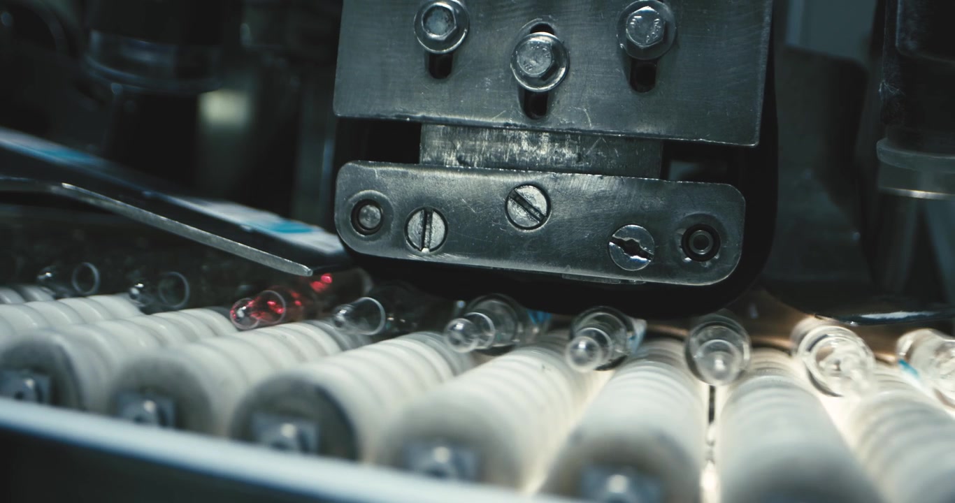Close-up of an industrial machine processing glass vials on a conveyor belt in a factory setting under bright lighting