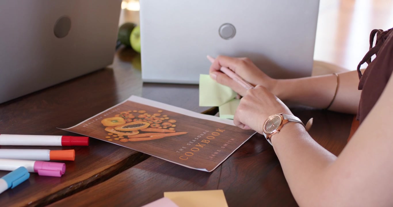 Mujeres asiáticas y afroamericanas, inspiradas por un libro de cocina en una mesa, etiquetando notas adhesivas, con espacio para texto