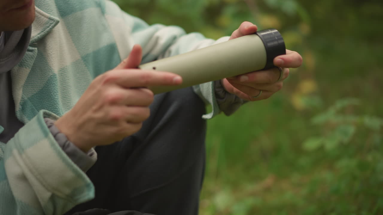 white camper retrieves yellow thermos, inspects monocular lens and extends spotting tube, then scans distant canopy relaxed exploration vibe, camp pause and subtle nature observation on trail