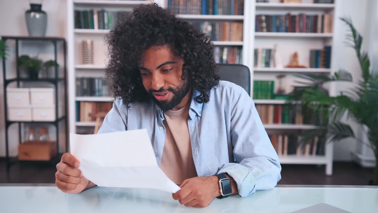 Overlykkelig succesfuld ung arabisk mandlig freelancer nyder at læse et papirbrev.