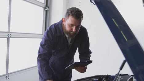 mecánico masculino en el garaje usando software de diagnóstico en una tableta digital para reparar el motor del coche